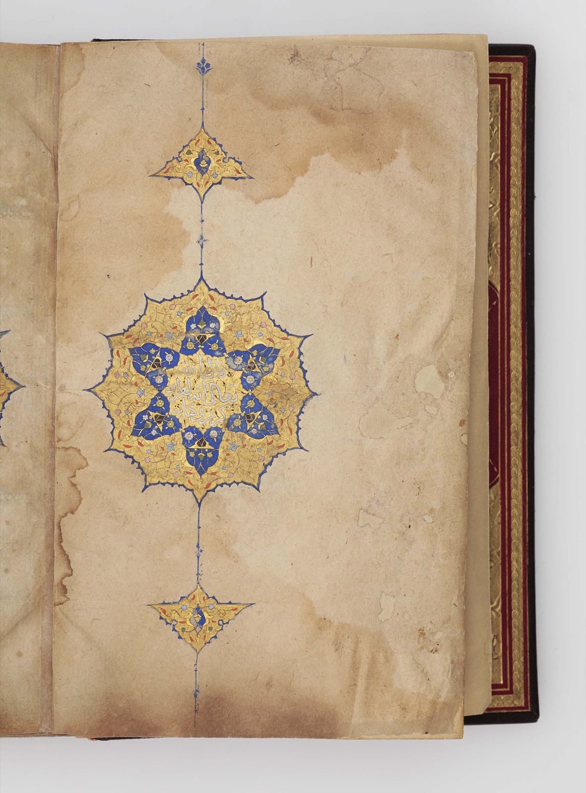 An illuminated Qur'an manuscript opened to a gold and lapis medallion on aged parchment.